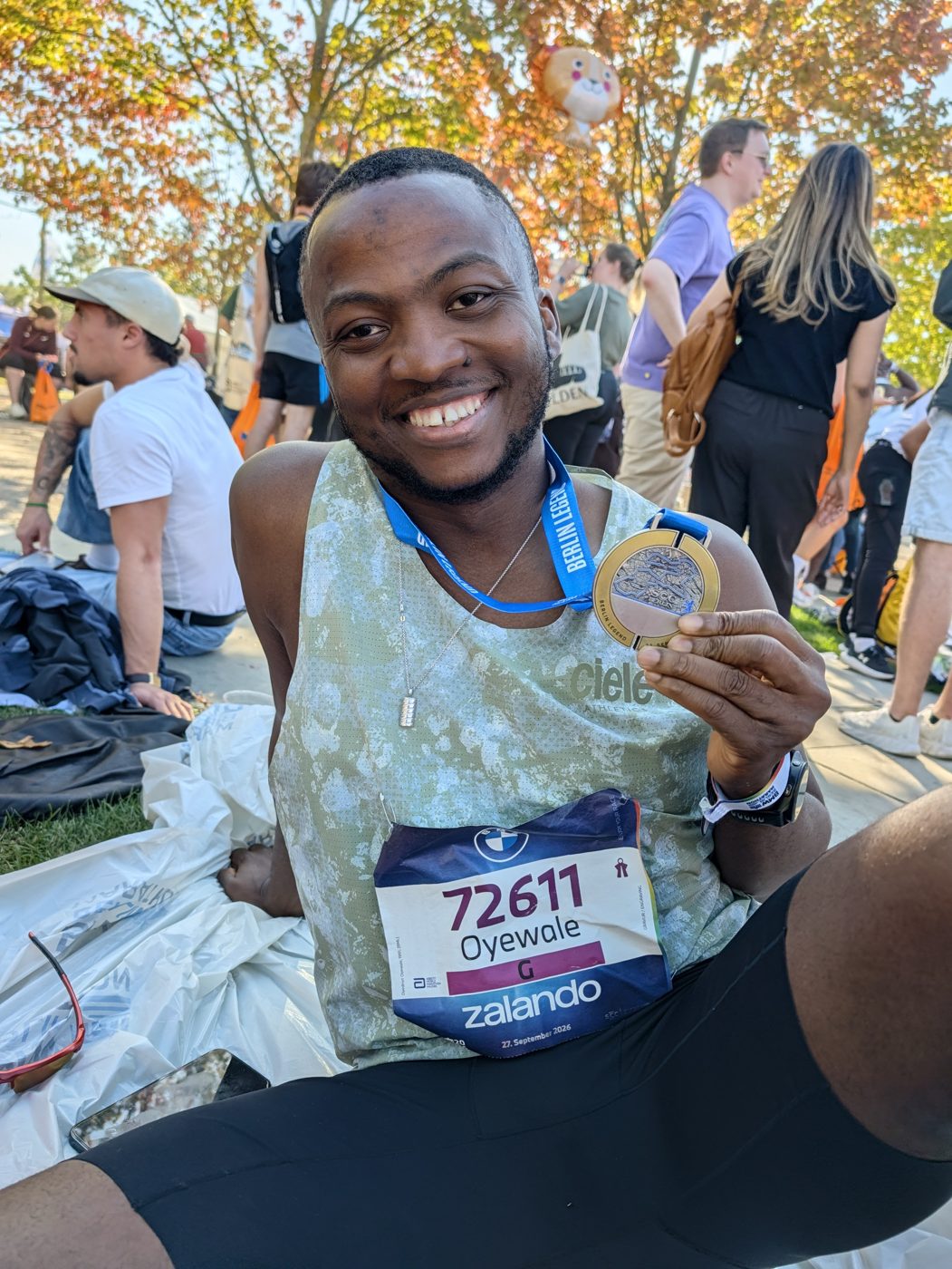 Oyewale sitting on the grass after the race, smiling and holding up his medal